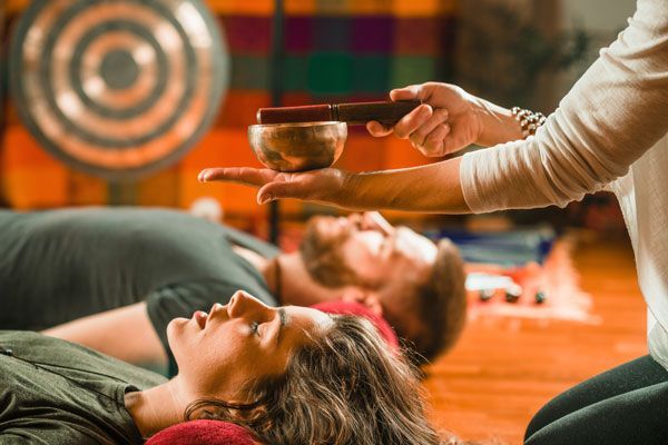 A woman is holding a singing bowl over a man and a woman laying on the floor.