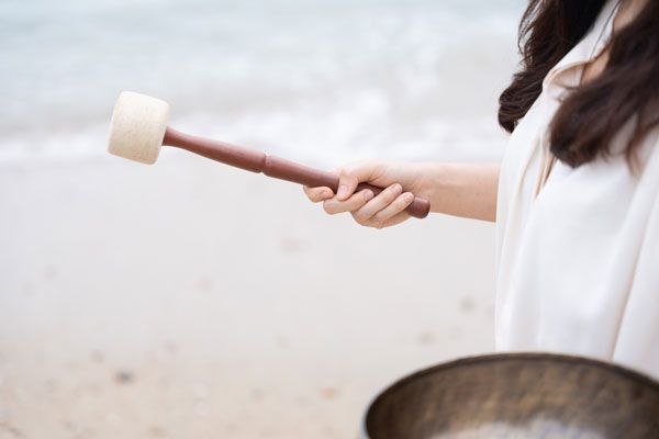 A woman is holding a wooden mallet over a bowl on the beach.