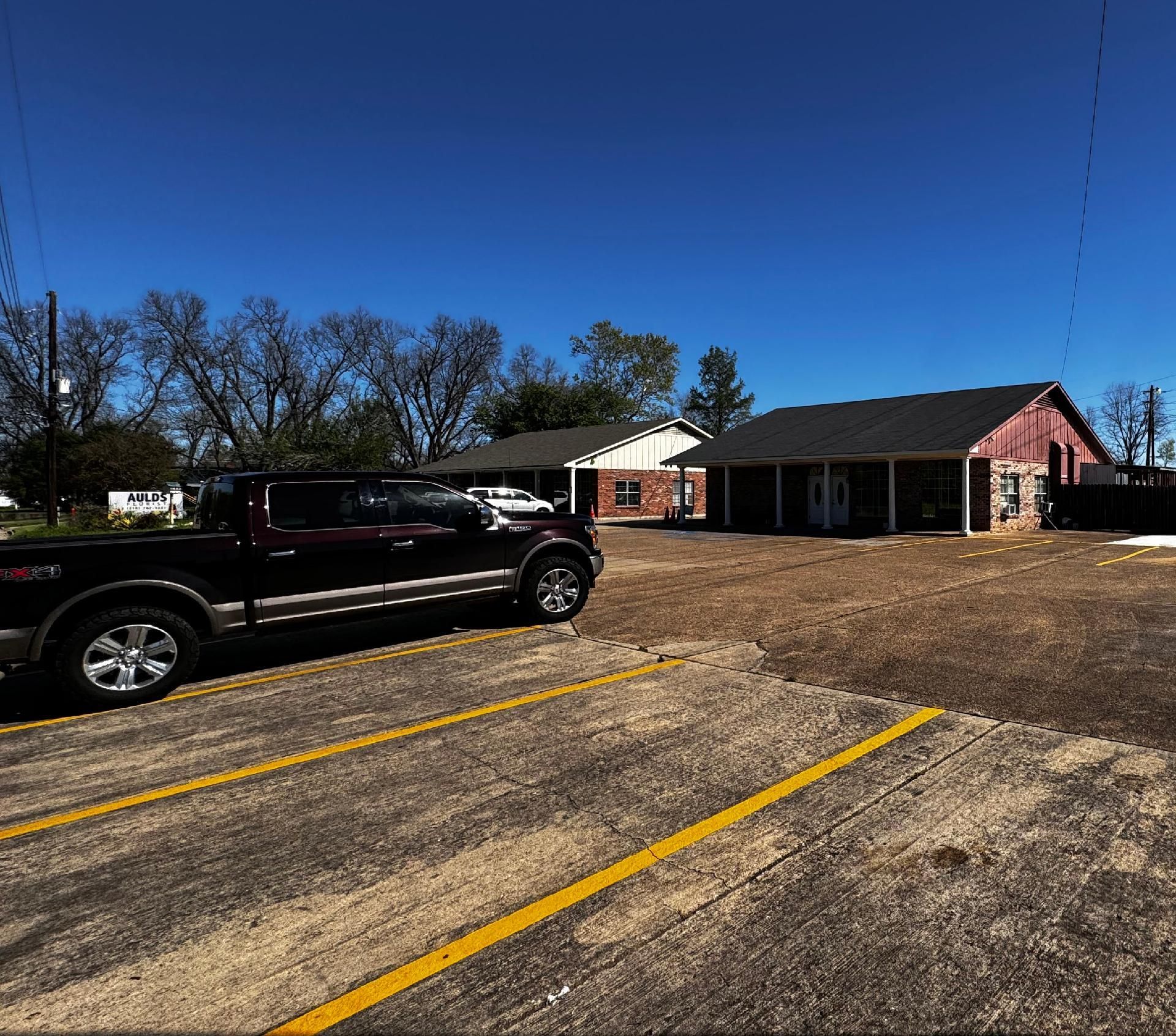 Dark pickup truck parked in a gravel lot with buildings in the background under a blue sky.