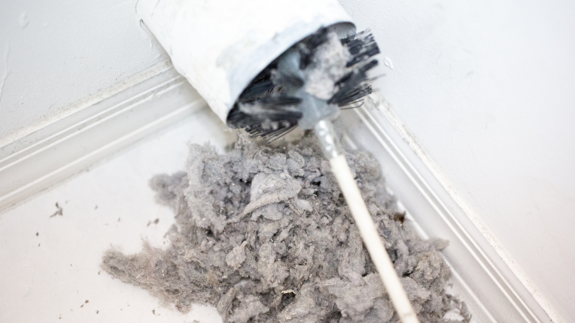 A person cleaning a lint-filled dryer vent with a brush, against a white background.