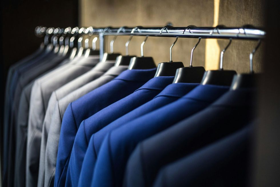 A row of suits hanging on a rack in a closet.