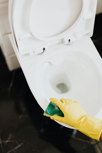 A person wearing yellow gloves is cleaning a toilet with a green sponge.