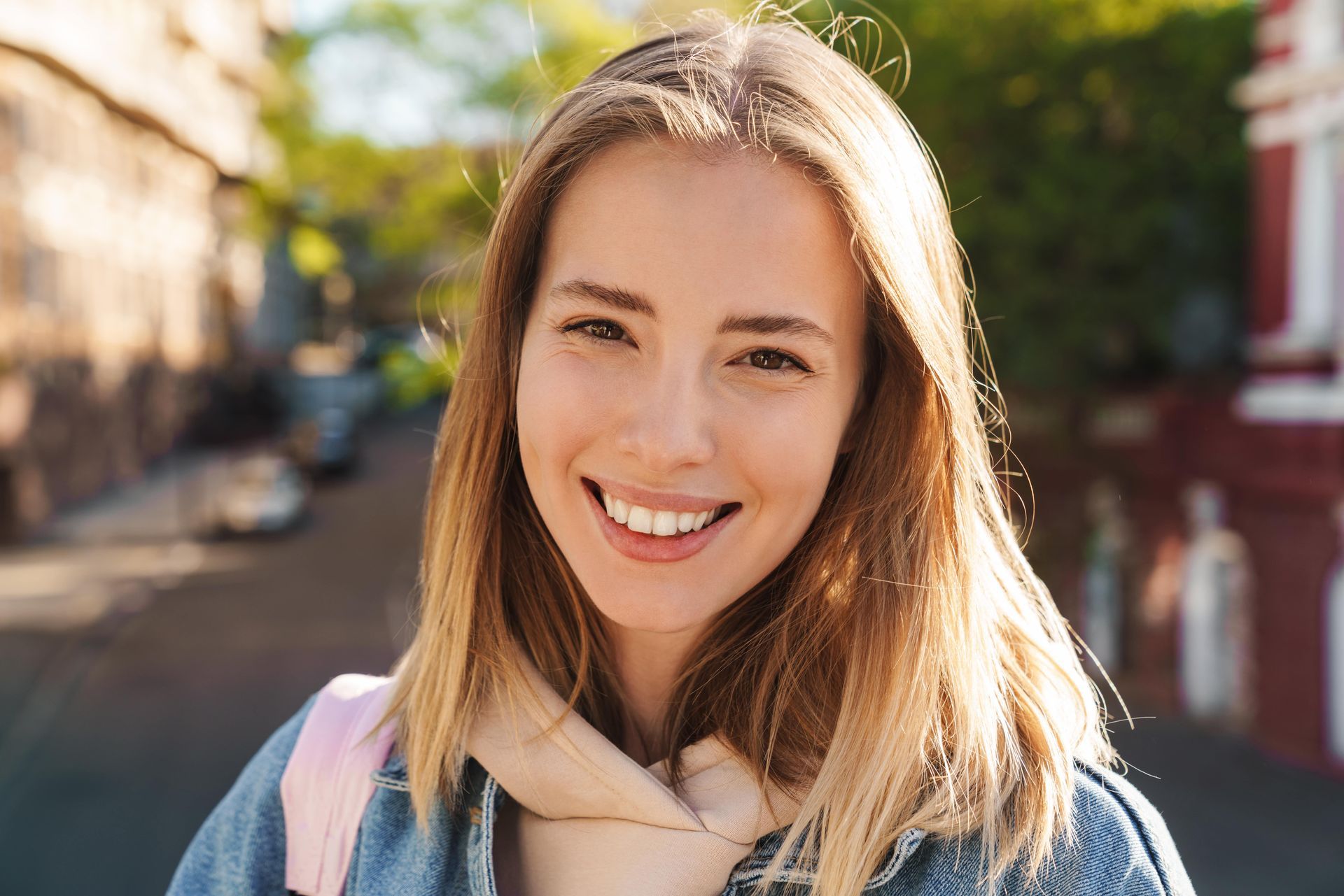 A young woman is smiling while standing on a city street.