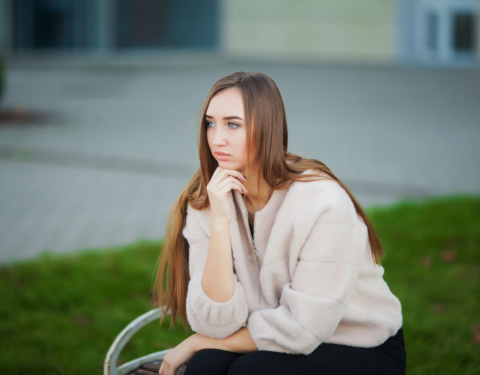 A woman is sitting on a bench with her hand on her chin.