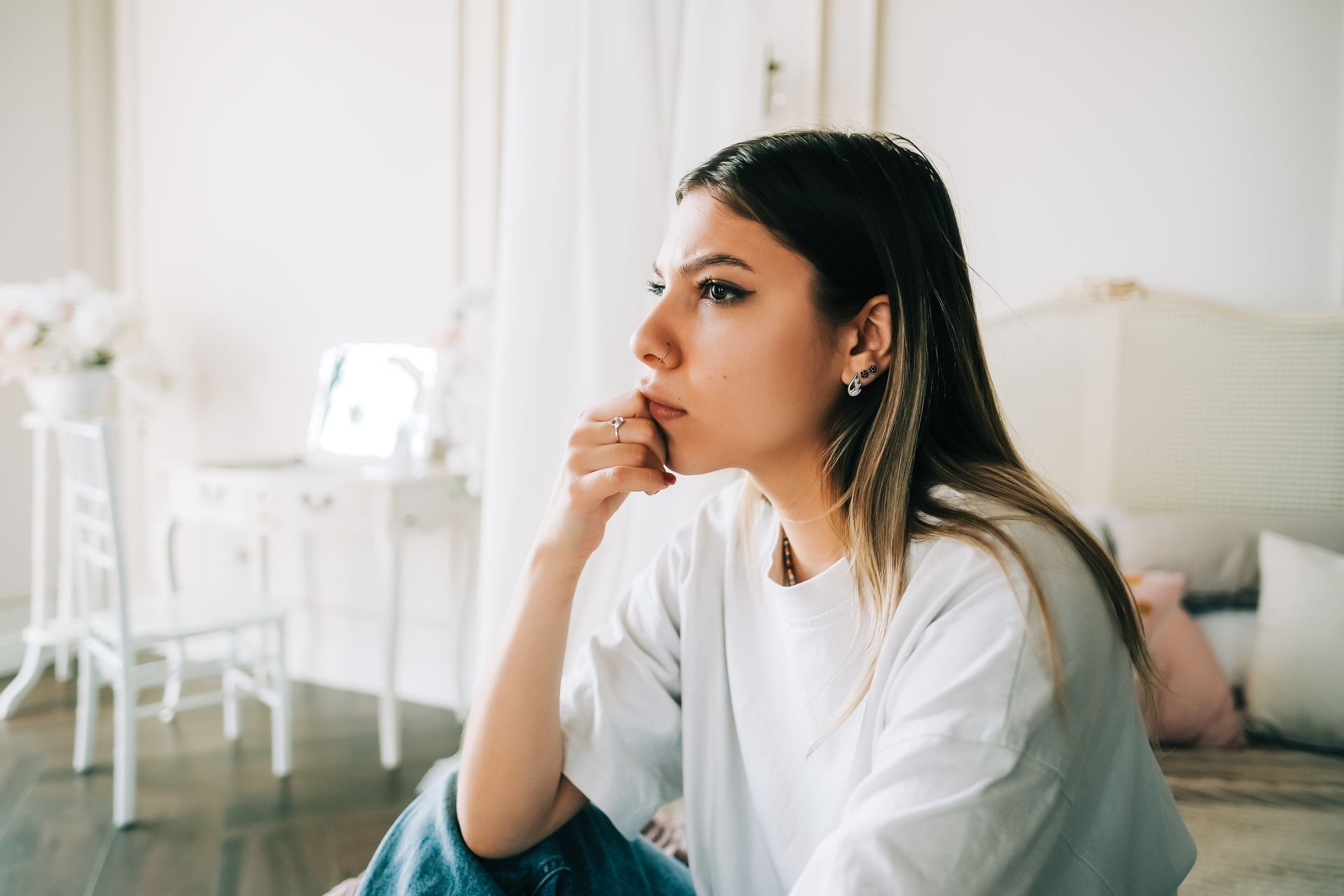 A woman is sitting on the floor with her hand on her chin.