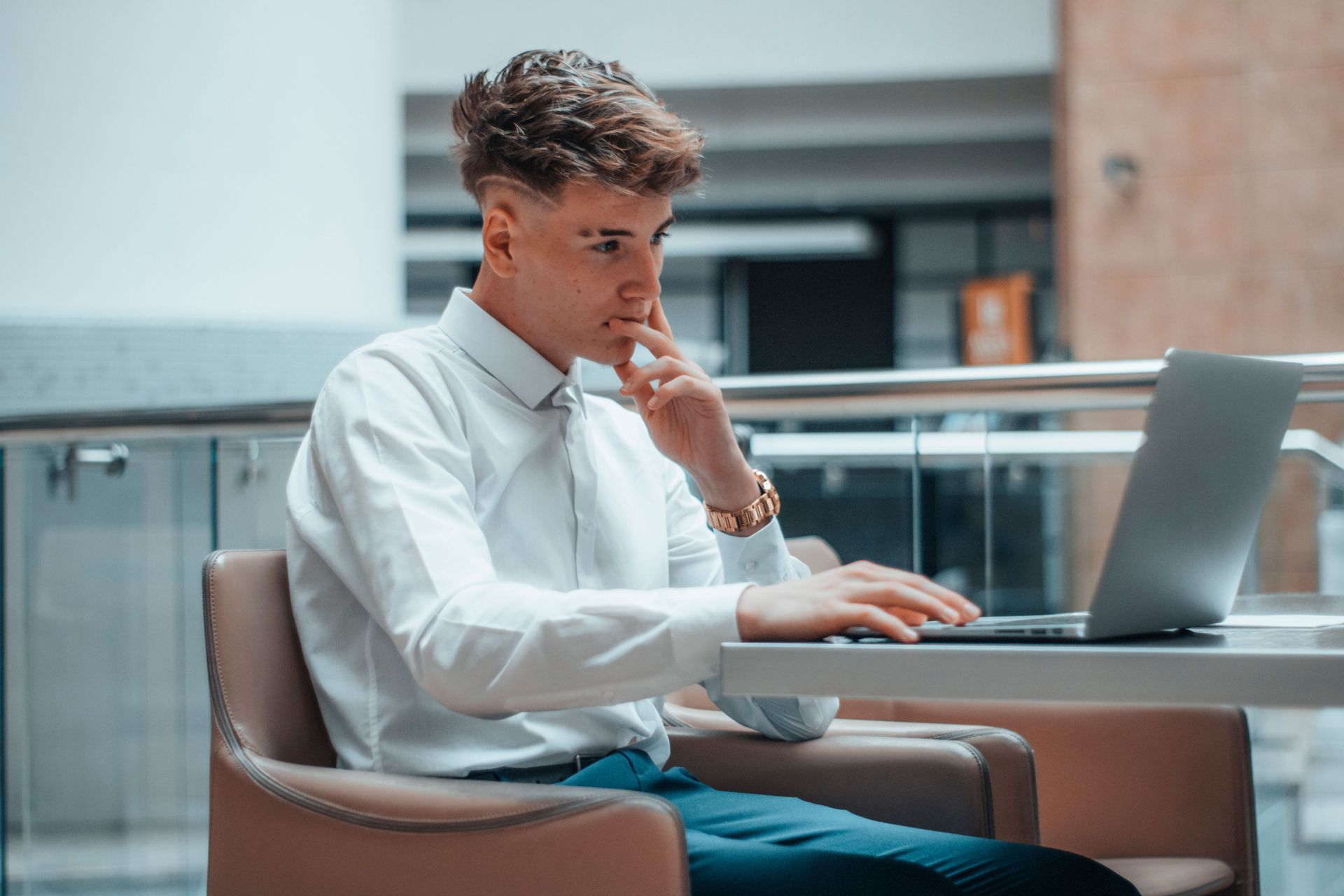 A young man is sitting at a table using a laptop computer.