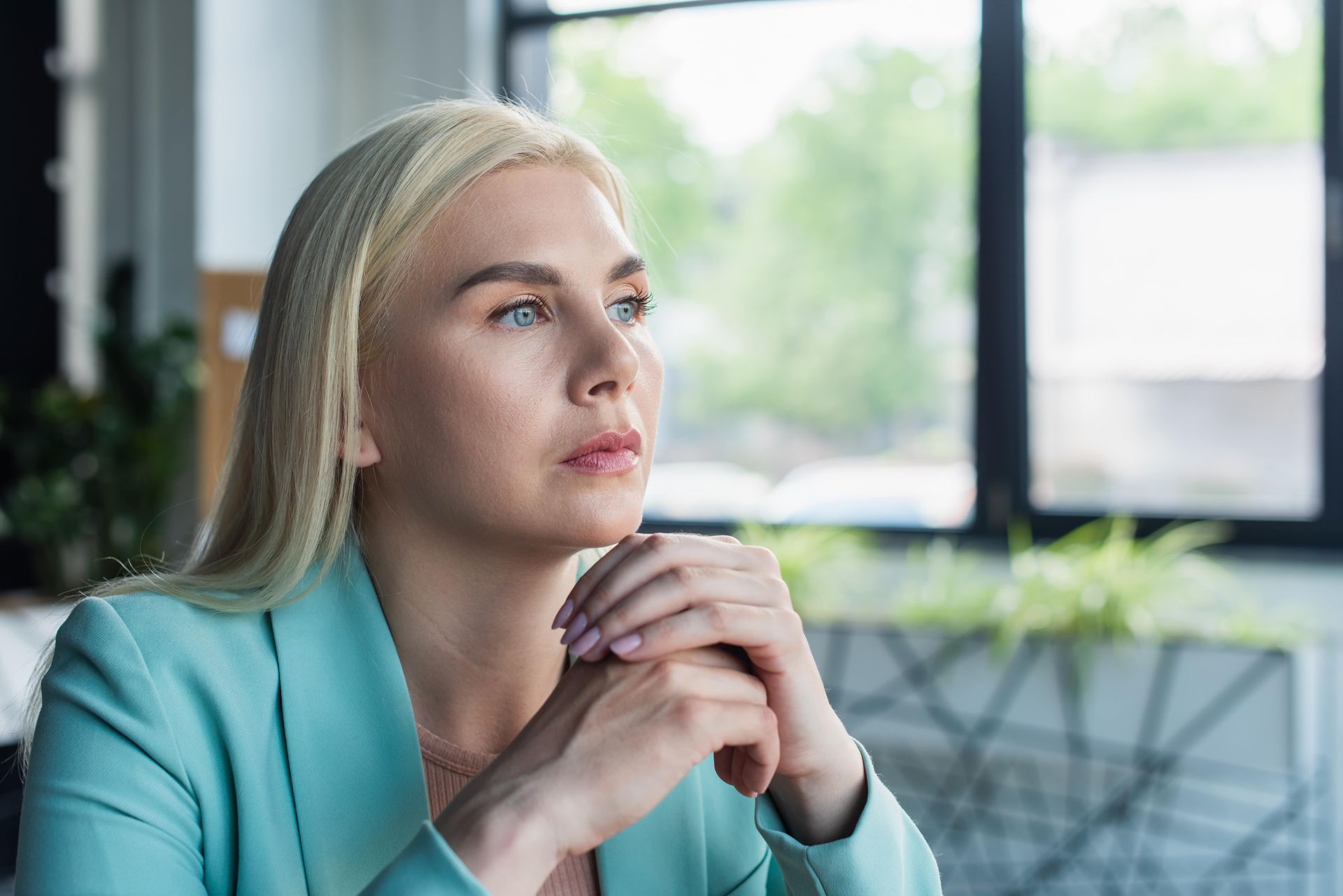 A woman is sitting in front of a window with her hands folded.