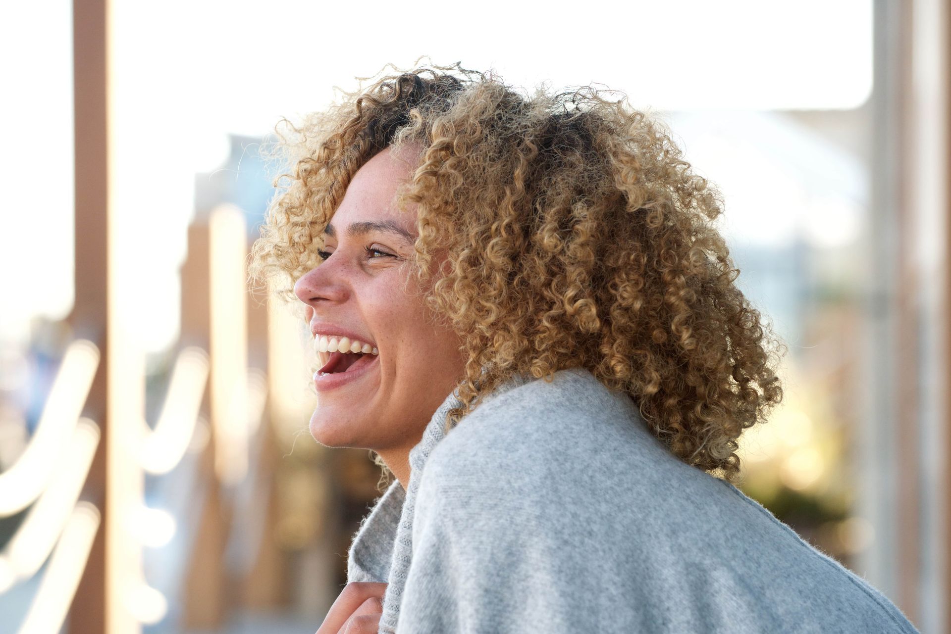 A woman with curly hair is laughing with her mouth open.