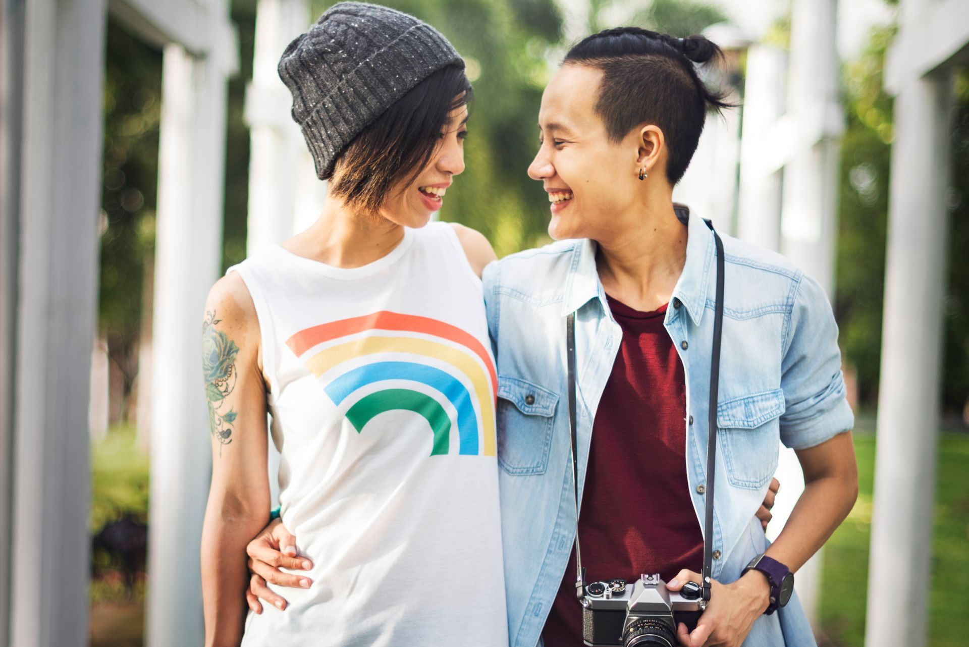 A couple of women standing next to each other in a park . one of the women is wearing a rainbow shirt.