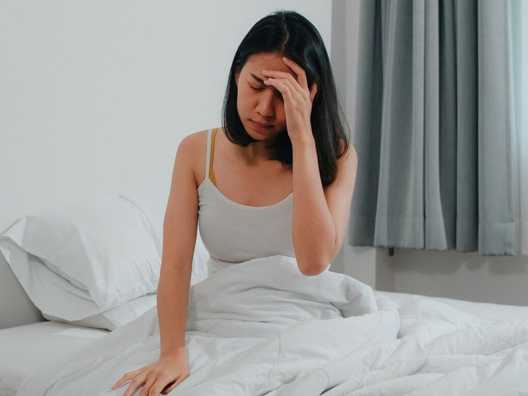A woman is sitting on a bed with her hand on her forehead.