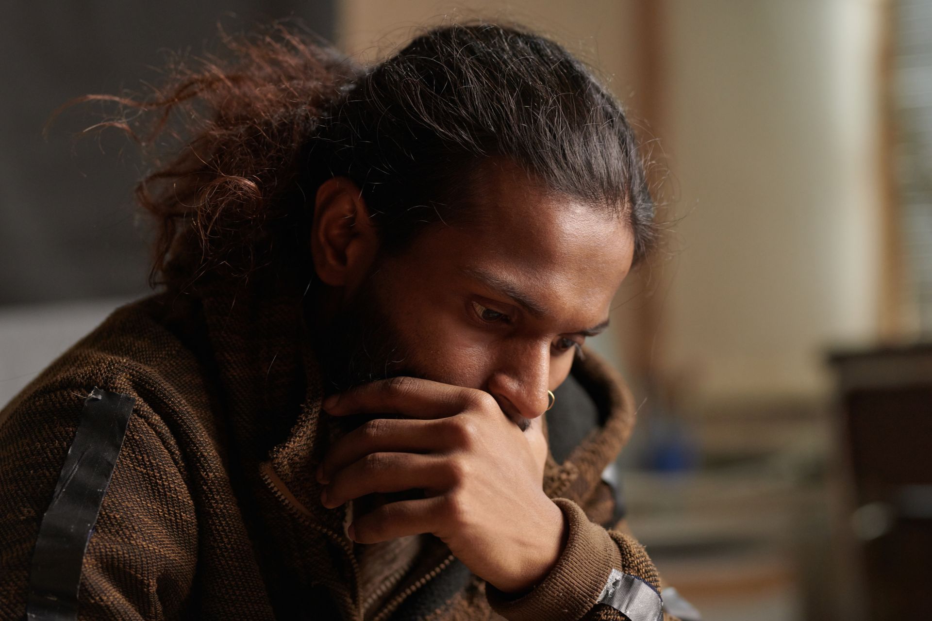 A man with a beard is sitting on a couch with his hand on his chin.