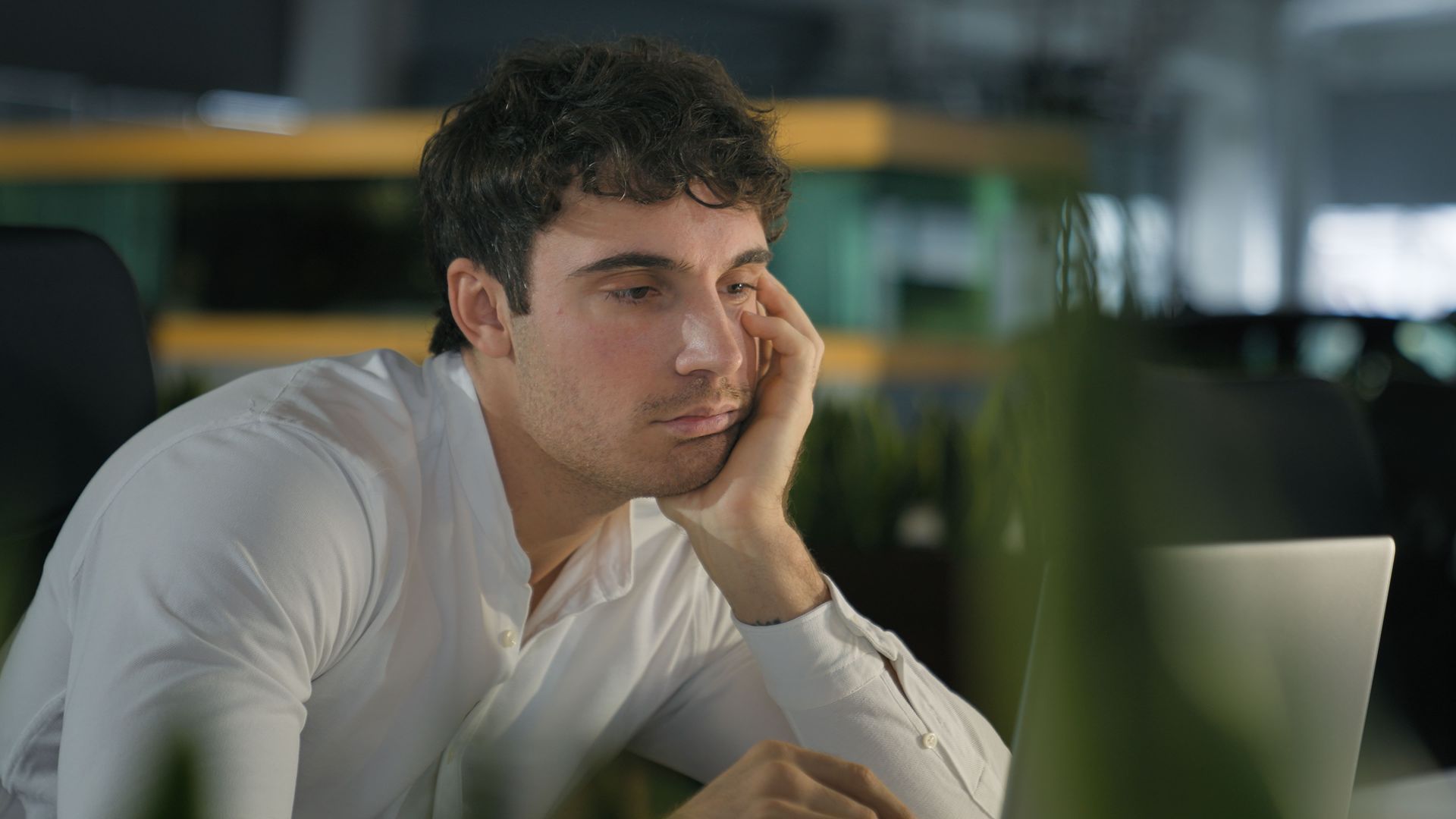A man is sitting at a desk looking at a laptop computer.