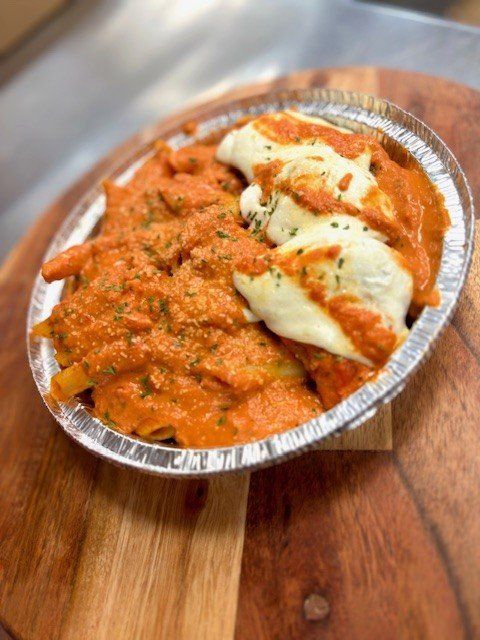 Pasta with tomato sauce and melted cheese in a foil container on a wooden surface.