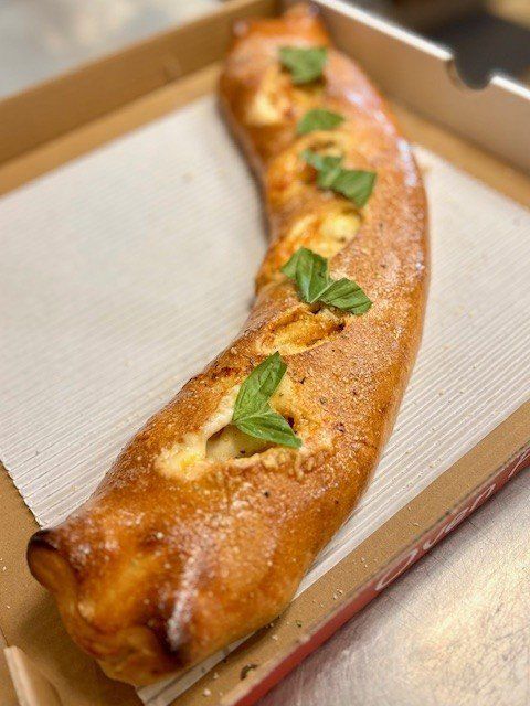 Calzone in a pizza box, golden brown with cheese peeking out, garnished with basil.