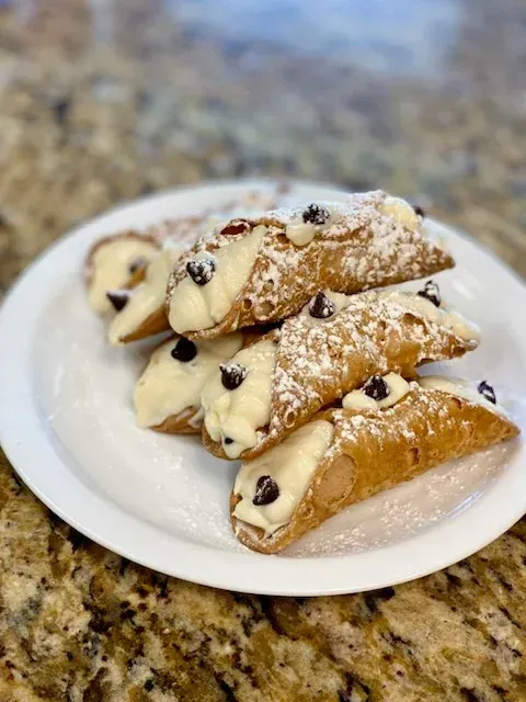 Cannoli pastries on white plate, dusted with powdered sugar and topped with chocolate chips.
