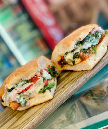 Two halves of a sandwich on a wooden board; filled with vegetables, melted cheese, and sauce.