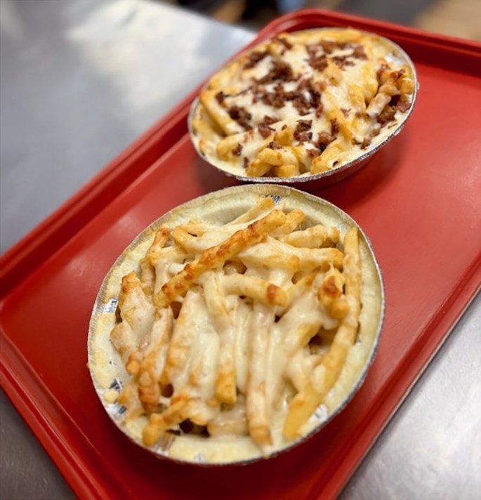 Two oval dishes filled with cheesy fries on a red tray. One has bacon.