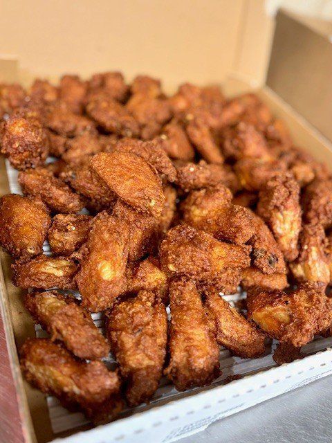Box of fried chicken wings, crispy and coated in a red-brown seasoning.
