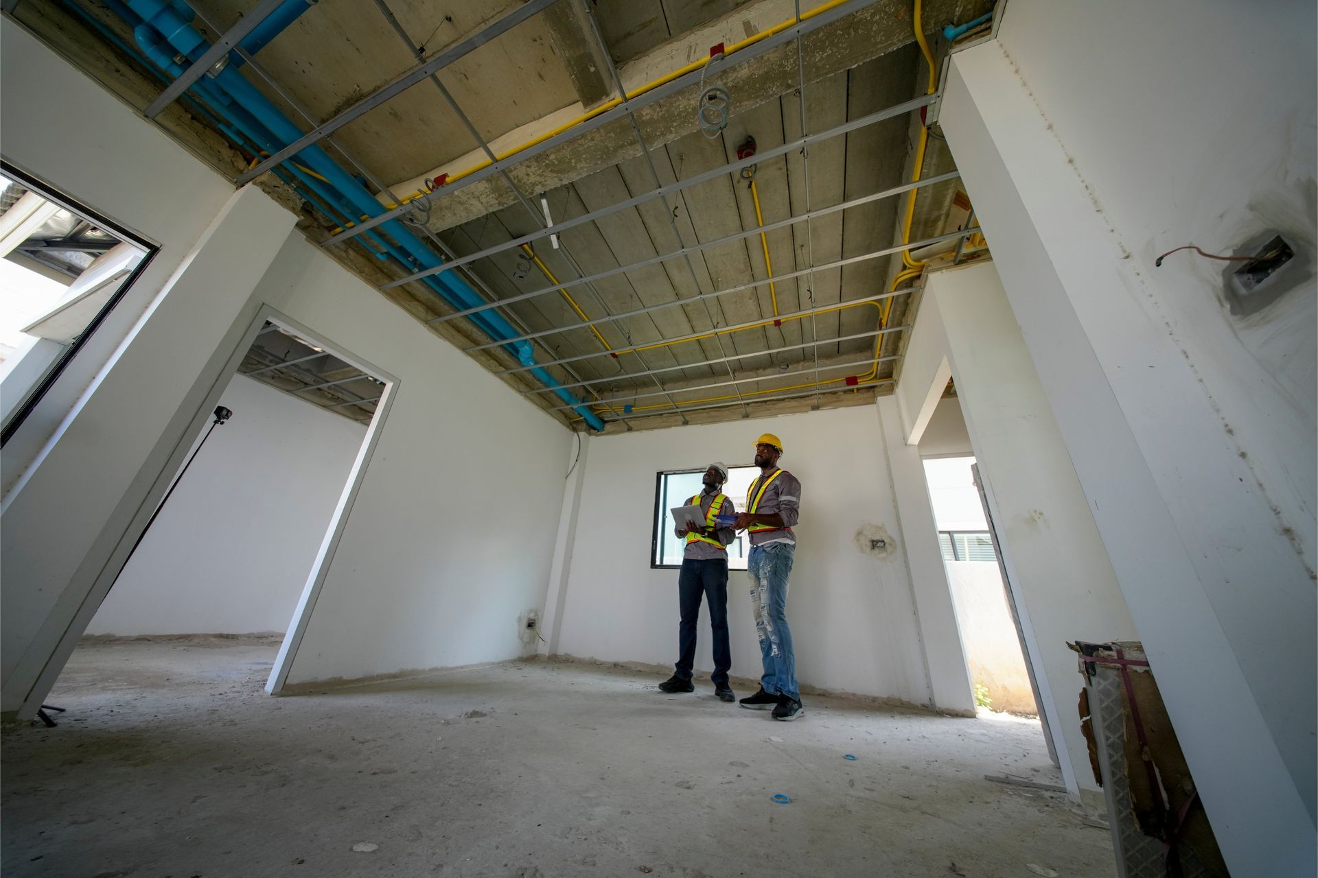 Two men in hard hats reviewing blueprints in a construction site interior.