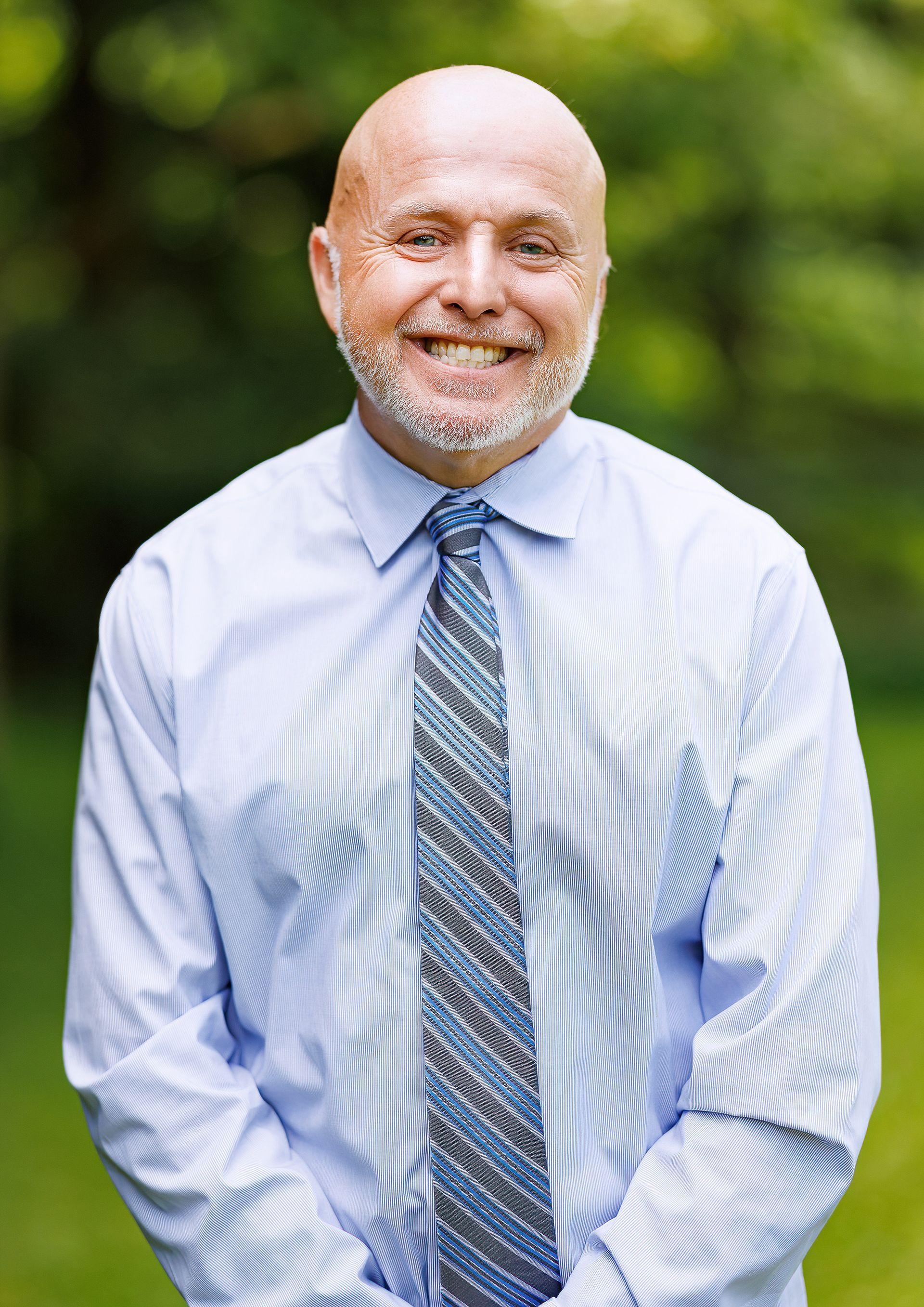 A bald man with a beard is wearing a blue shirt and tie.