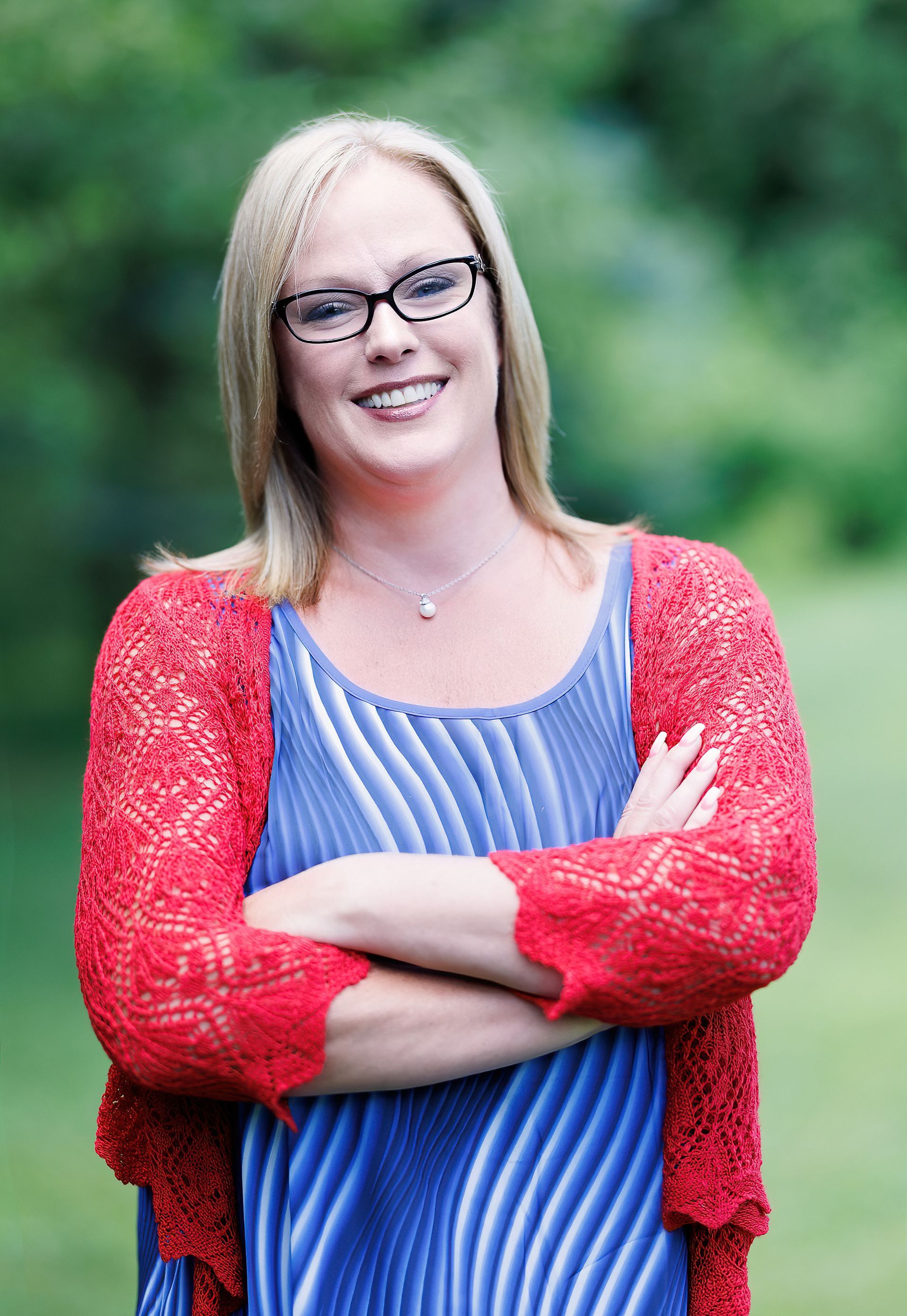 A woman wearing glasses and a red sweater is standing with her arms crossed.