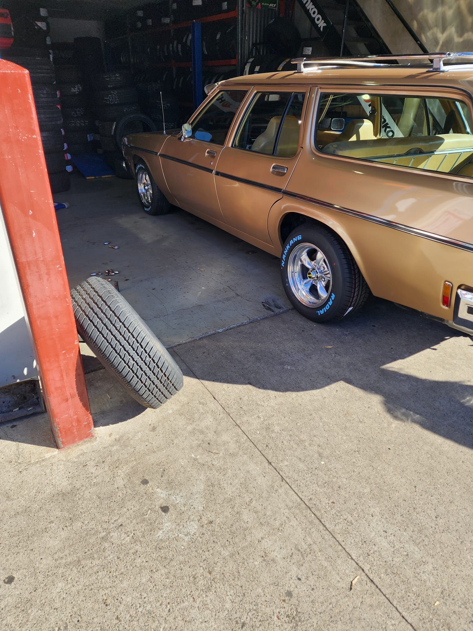 A Tyre Resting On A Wall And A car With Shiny Wheels in the background — Budget Tyre Shed In Charmhaven, NSW