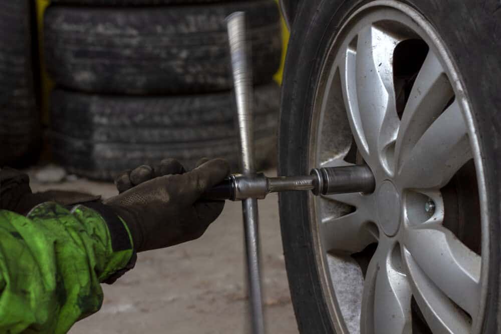 A Person Is Changing a Tire on A Car with A Wrench — Budget Tyre Shed In Charmhaven, NSW