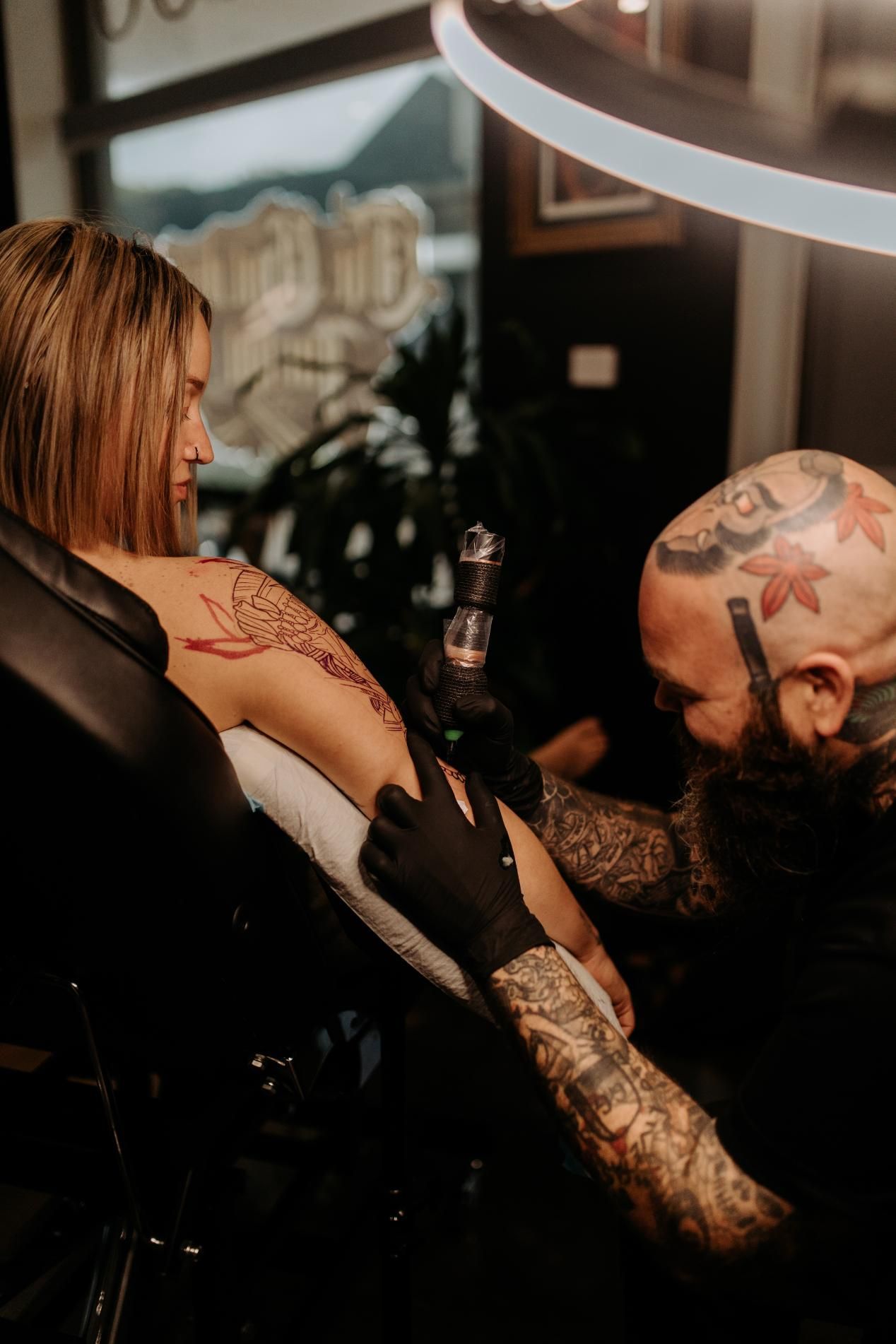 A Man is Tattooing a Woman 's Arm in a Tattoo Shop — Gallery Tattoo in Newcastle, NSW