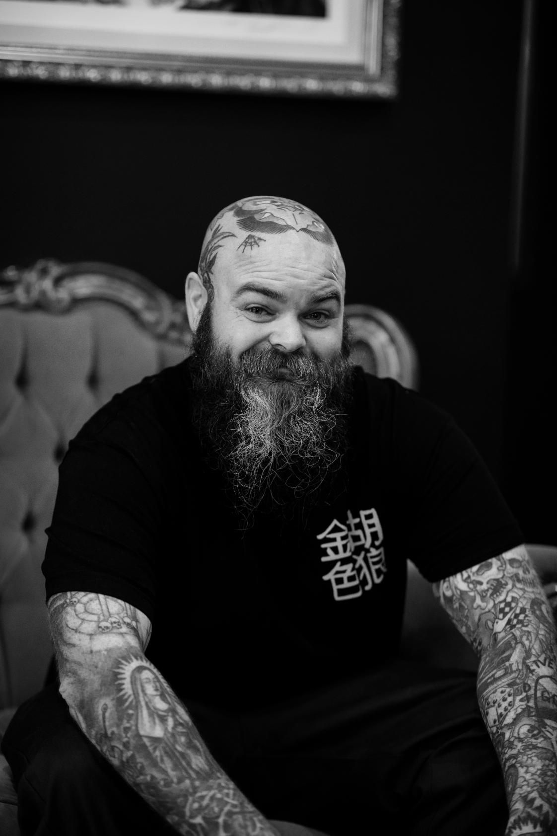 A Man With a Beard and Tattoos is Sitting on a Couch — Gallery Tattoo in Nelson Bay, NSW