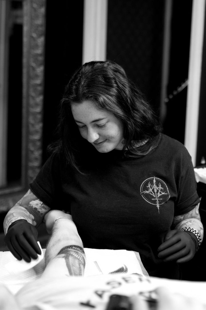 A Woman in a Black Shirt is Sitting at a Table Holding a Piece of Paper — Gallery Tattoo in Newcastle, NSW