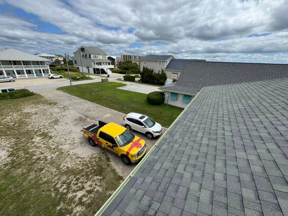 Aerial view of two cars parked beside a house in a coastal neighborhood with cloudy skies.