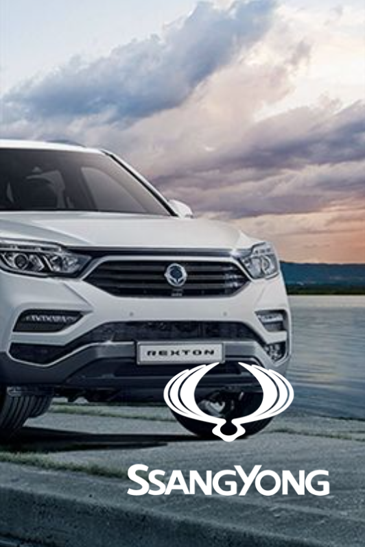 White SsangYong Rexton SUV parked on pavement with the brand's logo in the foreground. Sky background.