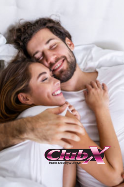 Couple cuddling in bed, both smiling. White sheets and t-shirts. Club X logo.