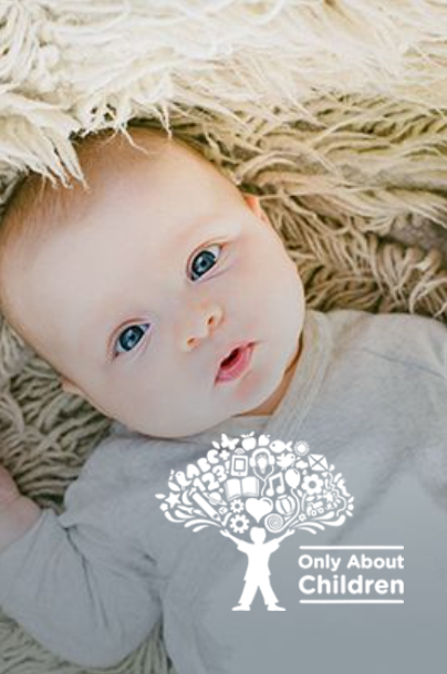 Baby lying on a textured surface, looking at the camera. 