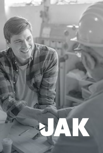 Two men shaking hands in a workshop. One man is smiling. The word 