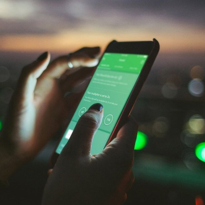 Hands holding a smartphone with a green screen, set against a blurred city skyline at dusk.