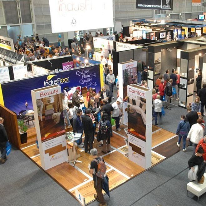 Trade show floor with various booths and people. Wood flooring on display, attendees browsing.