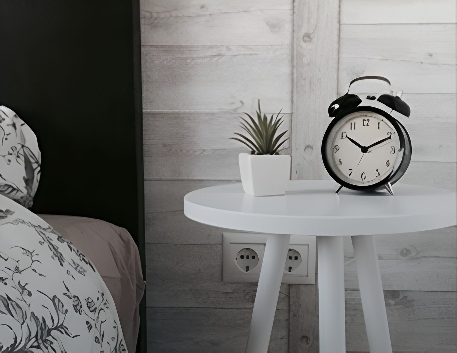 White nightstand with alarm clock and plant next to a bed in a bedroom.