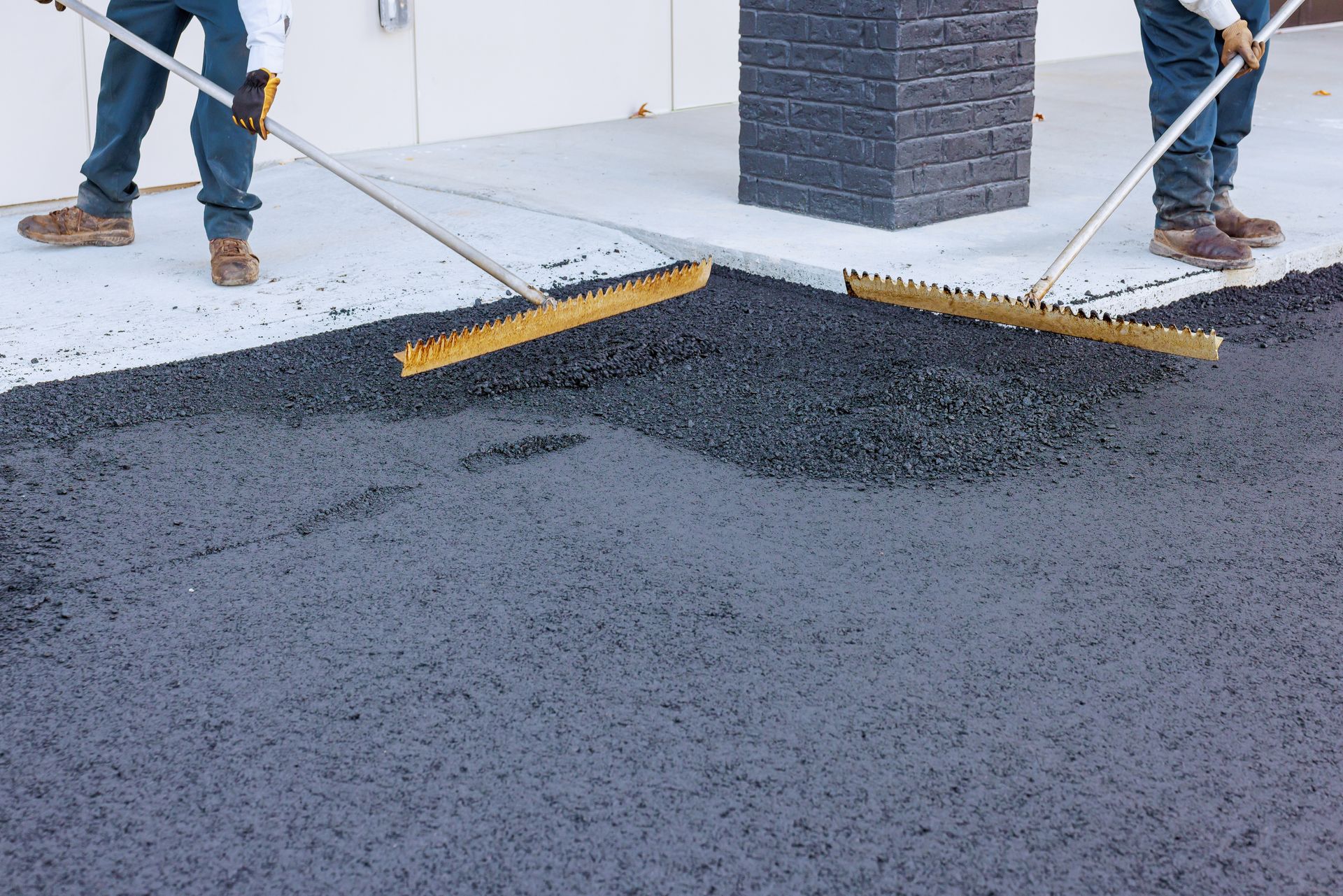 Two workers using rakes to spread and level fresh asphalt during paving work Two workers using rakes to spread and level fresh asphalt during paving work