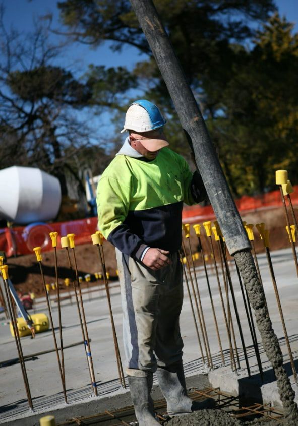 A Man Is Standing Next To A Concrete Pump On A Construction Site — Heritage Concrete In Uralla, NSW
