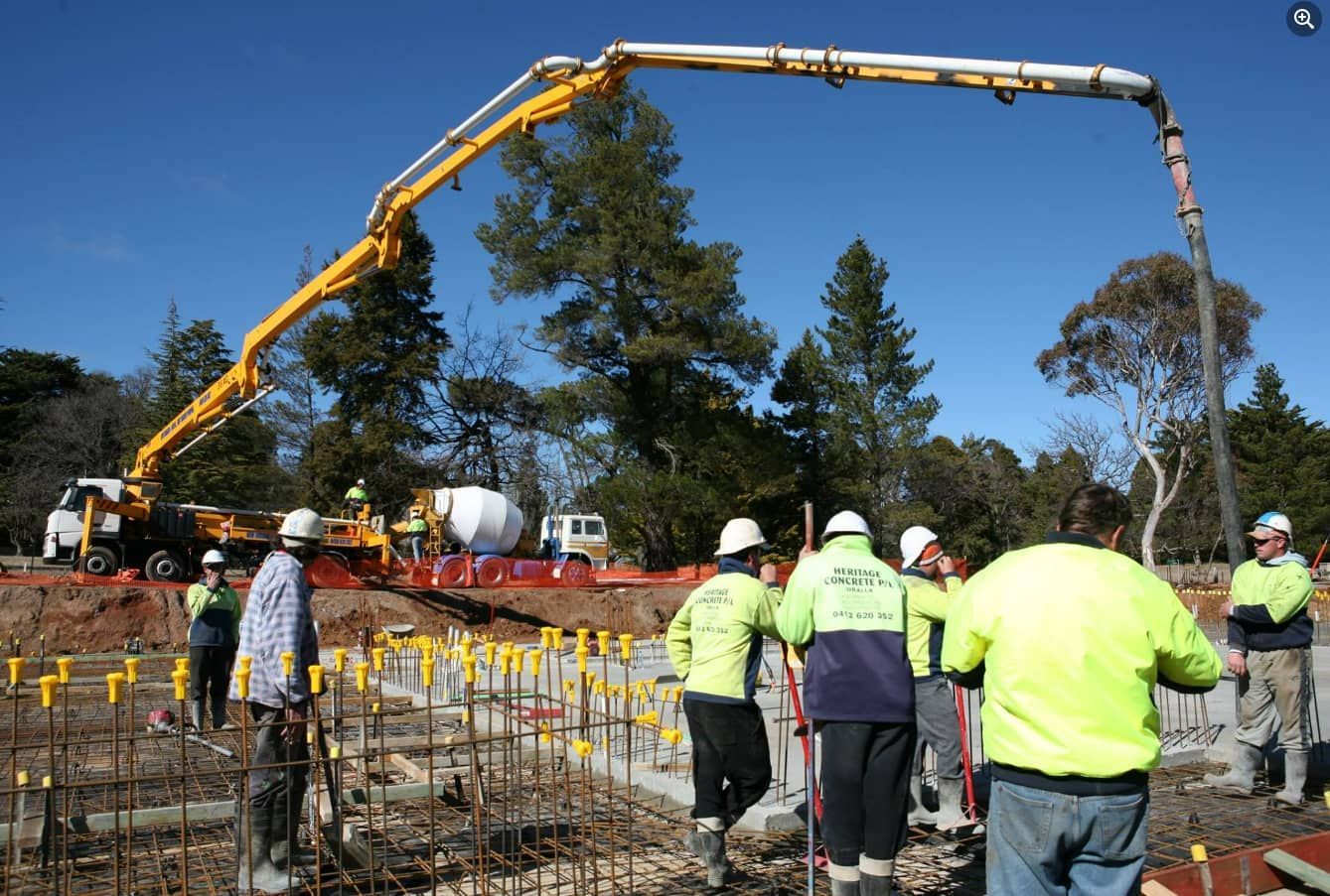 A Group Of Construction Workers Are Standing In Front Of A Concrete Pump — Heritage Concrete In Uralla, NSW