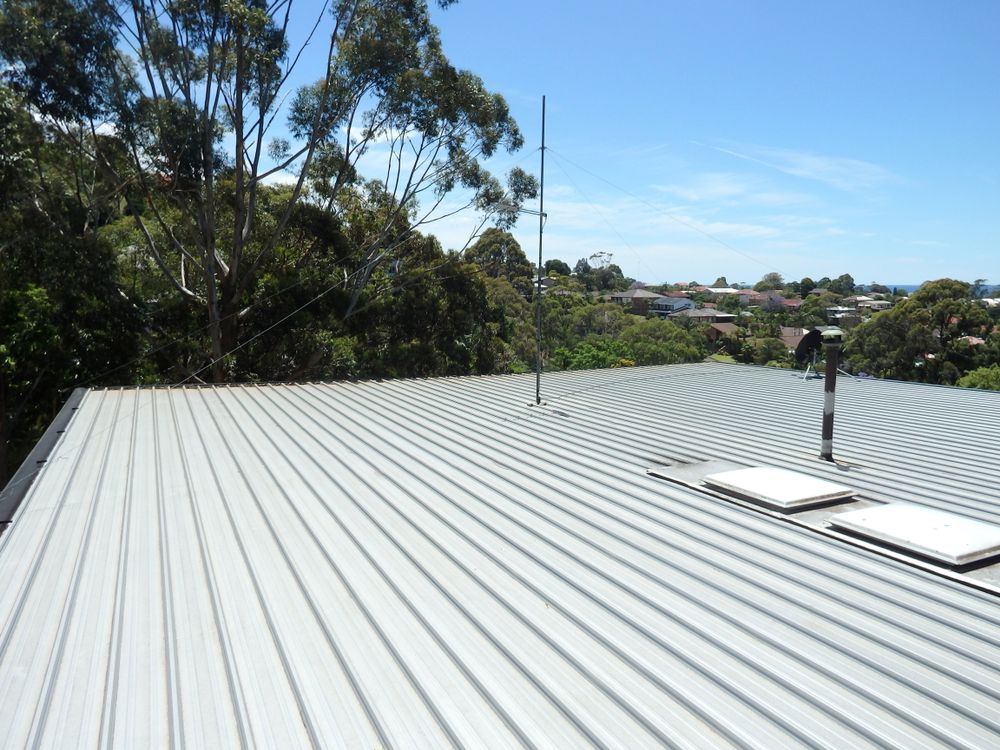 Workers in Safety Gear Installing Insulation on A Metal Roof Under a Hazy Sky — Hi Tech Roofing in Cessnock, NSW