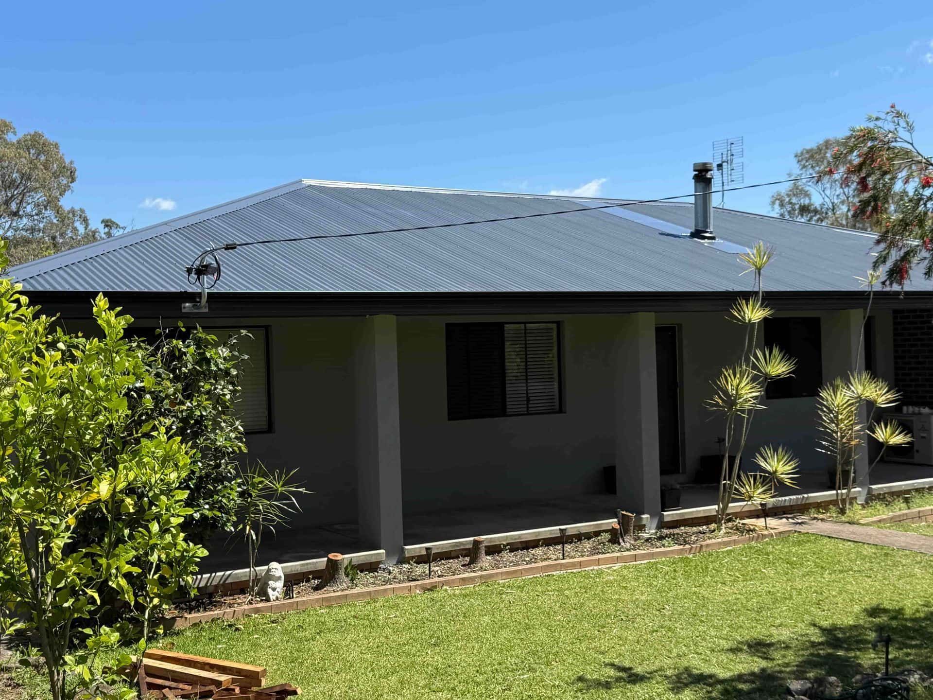 Gray house with a dark blue corrugated metal roof, front porch, and lawn.