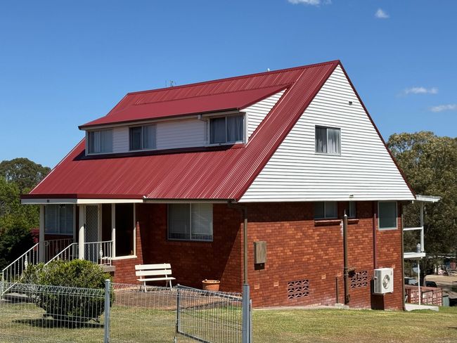 Two-story house with red metal roof, brick base, and white siding under a blue sky.