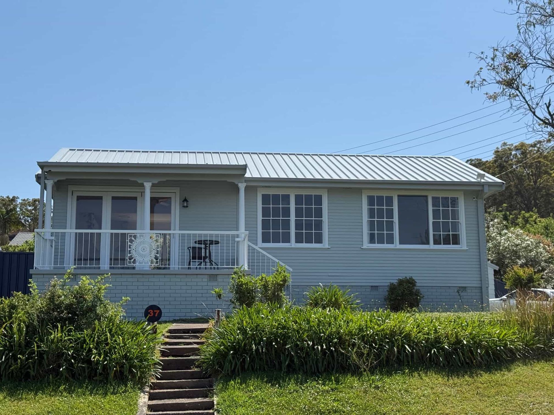 Light blue house with white trim, porch, and metal roof under a blue sky.