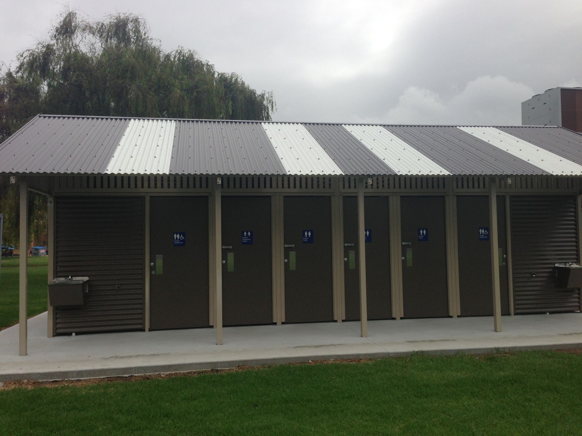 Public restroom building with gray and white striped roof and brown doors.