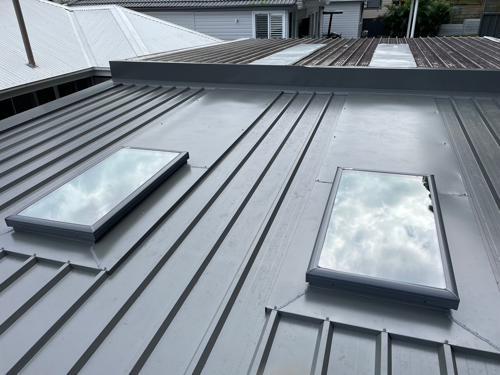 Grey metal roof with two rectangular skylights reflecting the sky.