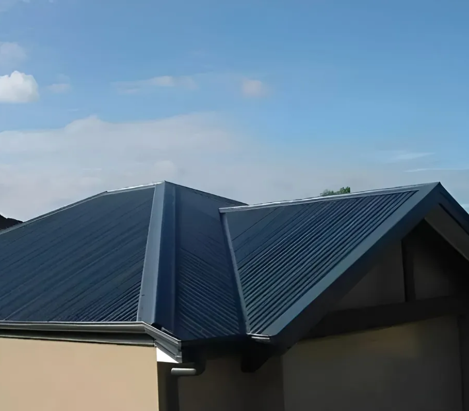 Blue Corrugated Metal Roof on A Light Tan Building Under a Partly Cloudy Sky — Hi Tech Roofing in Cessnock, NSW