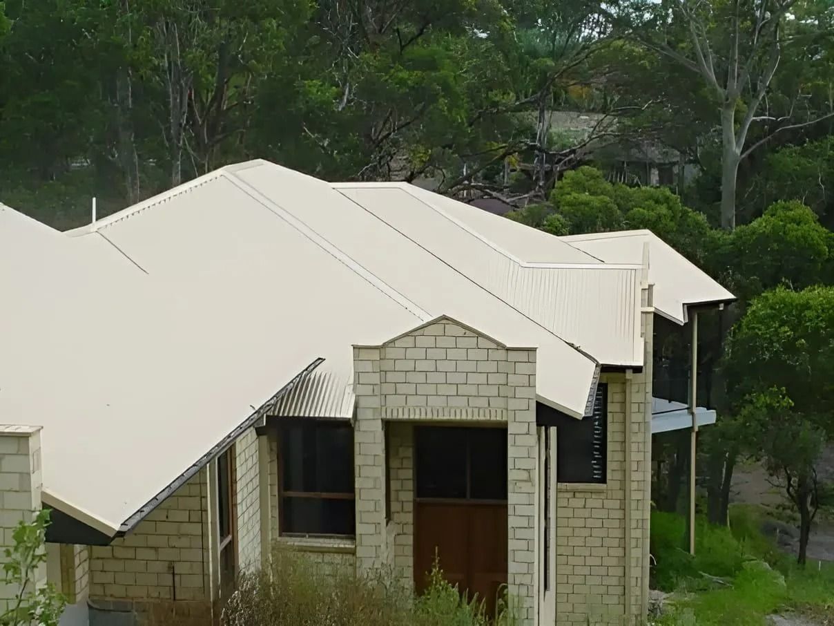 Beige Brick House with Matching Roof, Set Against a Backdrop of Green Trees — Hi Tech Roofing in Kilaben Bay, NSW