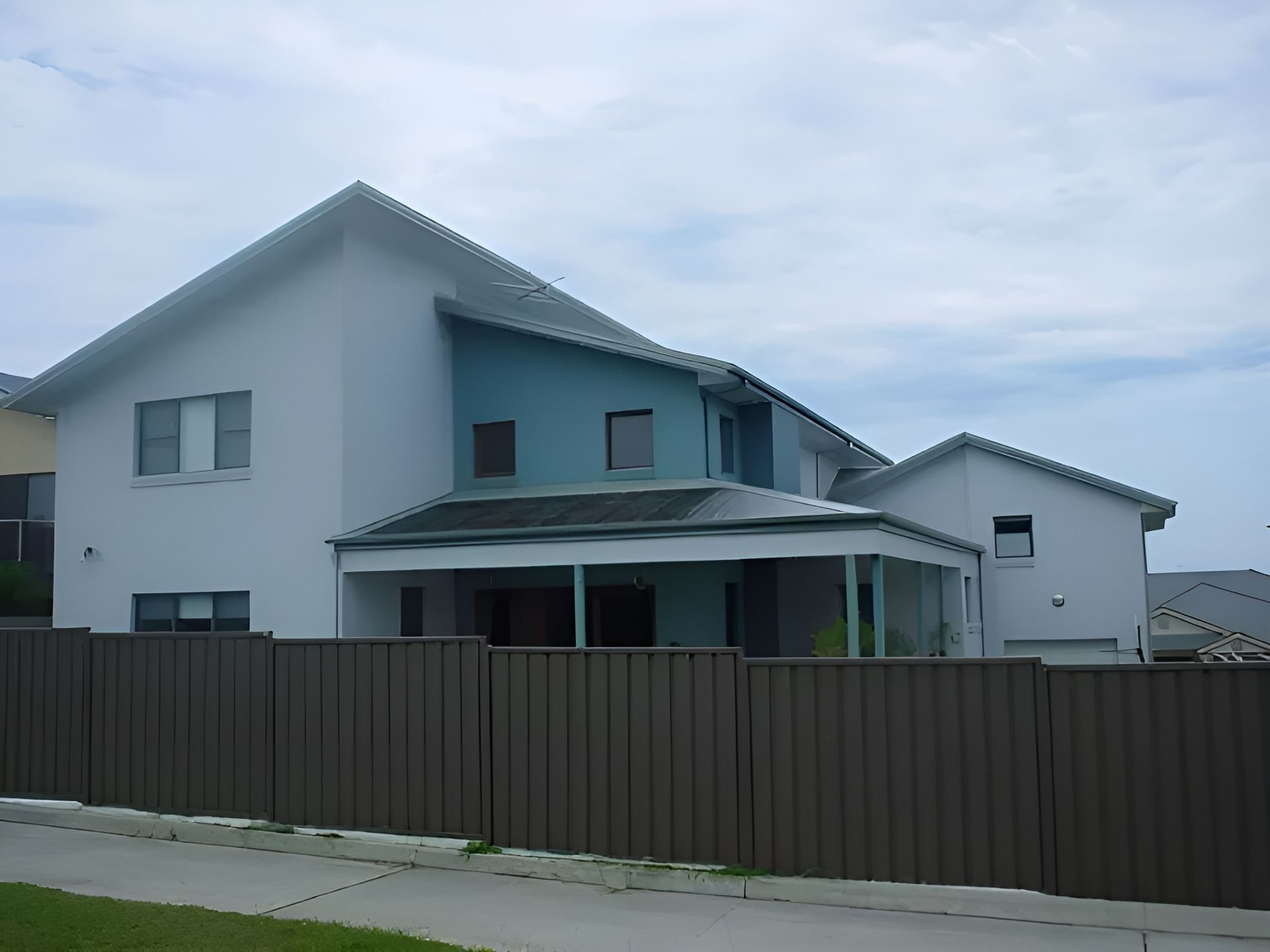Two-Story House with White and Blue Walls, Brown Fence, and Cloudy Sky — Hi Tech Roofing in Kilaben Bay, NSW